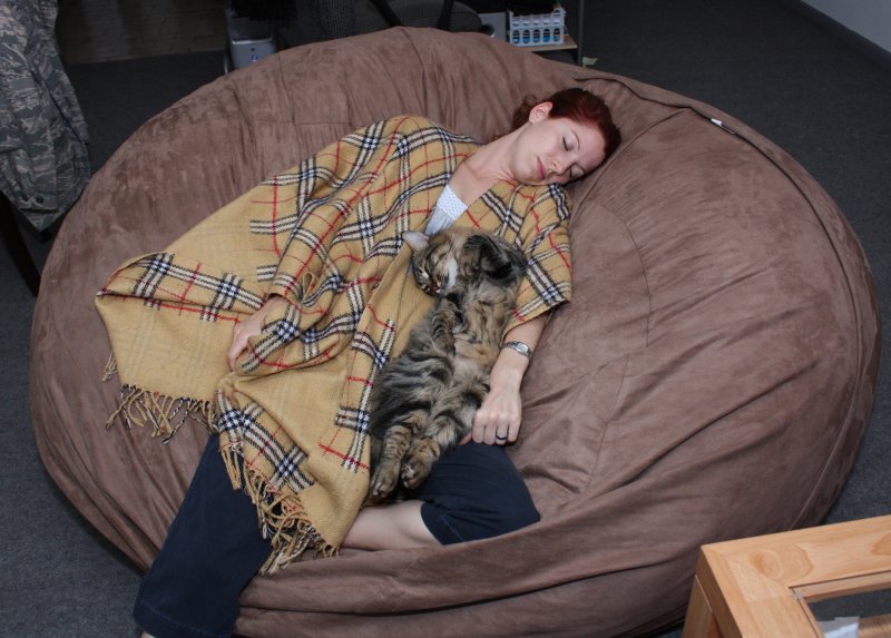A picture of a woman and her cat snuggling together on a brown, giant Fombag